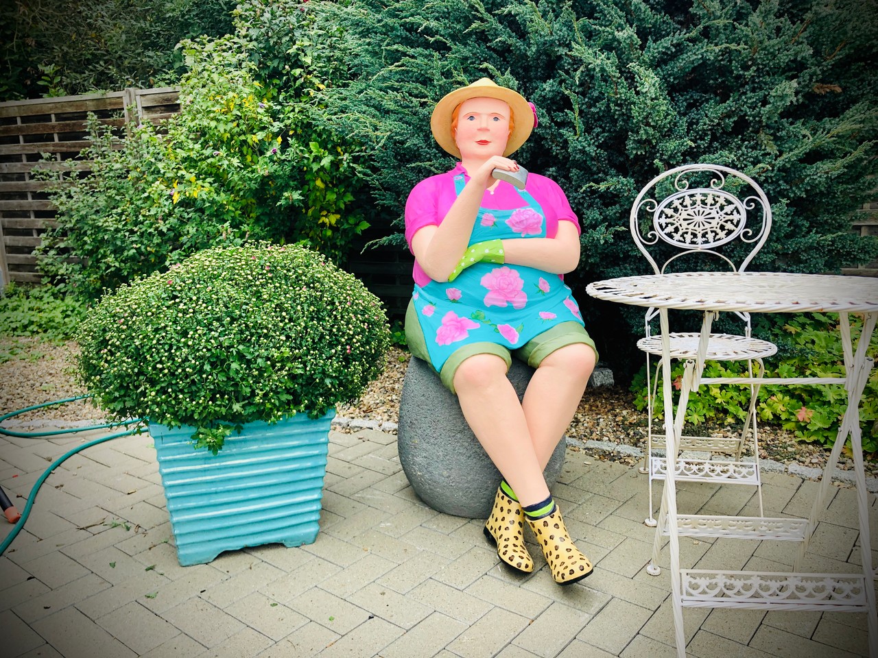 Farbig gekleidete sitzende Betonskulptur im Garten